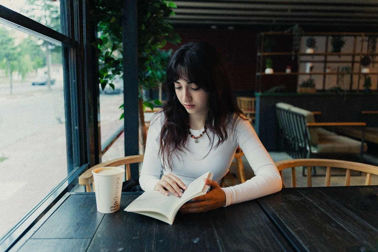 Young woman reading a book at a cozy café, enjoying a coffee and relaxed ambiance.