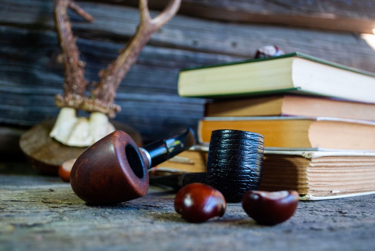 Cozy rustic setting featuring wooden pipes, stacked books, and antler decor on a wooden surface.